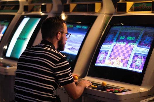 A man with striped t-shirt is playing on arcade video game.